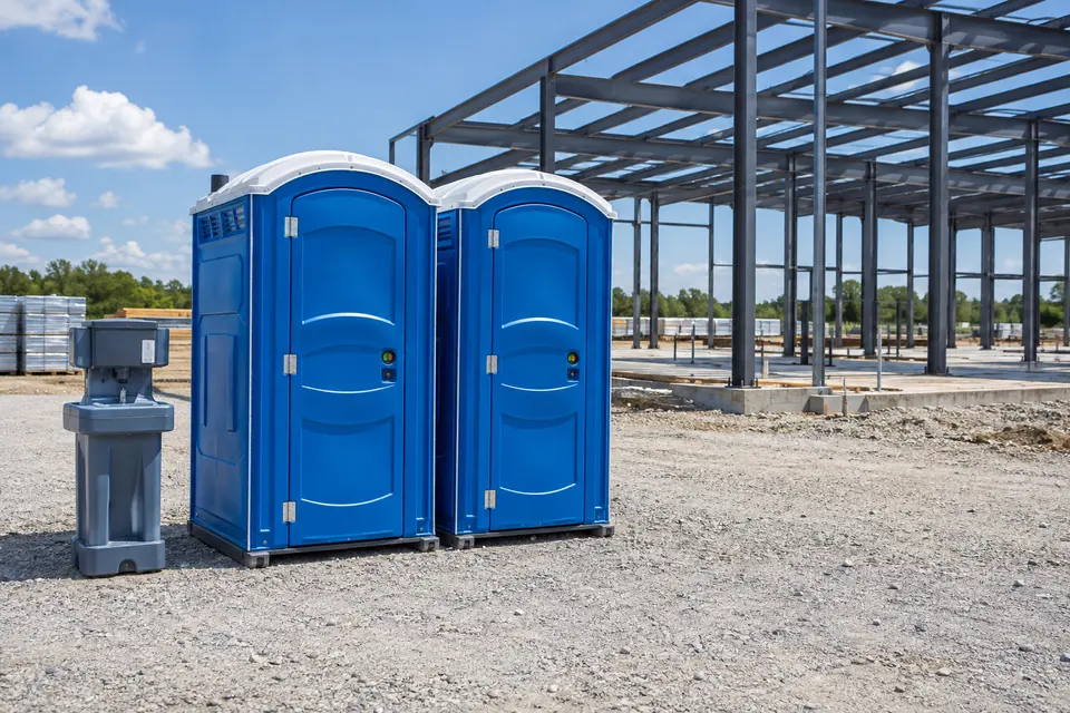 Portable toilets and a handwashing station beside a steel-frame construction site